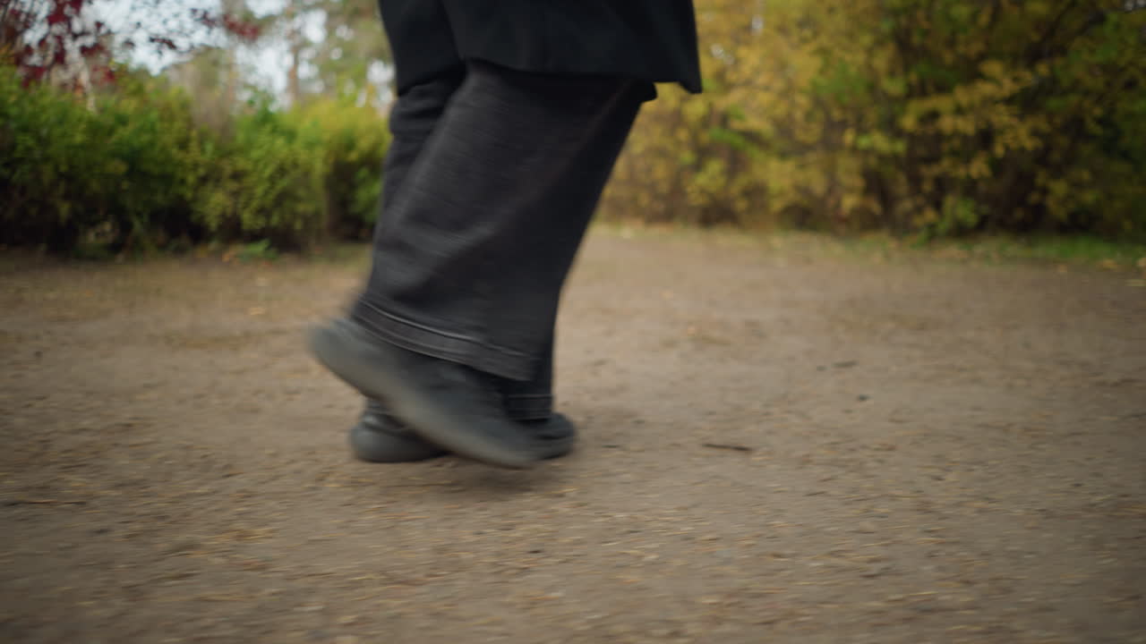 vista lateral dinámica de las piernas de una persona en vaqueros negros y zapatos de lona, capturando la esencia de un paseo de otoño a través de un jardín con follaje vívido y tonos terrenales