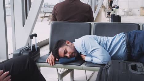 hombre de negocios durmiendo en los asientos en la sala de salidas del aeropuerto debido al retraso