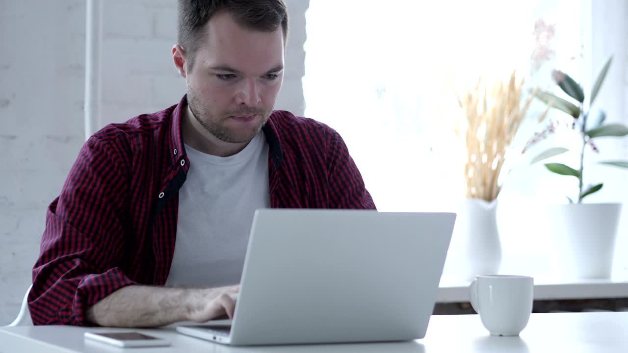 joven enojado trabajando en una computadora portátil en la oficina