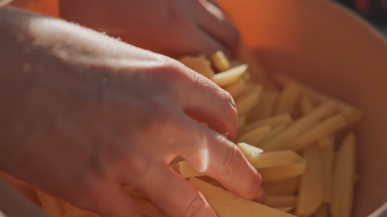 Hands mix raw potato pieces for cooking. Rustic outdoor kitchen with fresh potato fries in preparation. Vibrant camping scene with hands preparing crispy potato fries in rustic outdoor setting