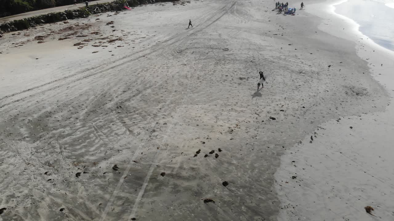 A drone flies above a surfer as he gets ready to head out to a fun day of surfing.