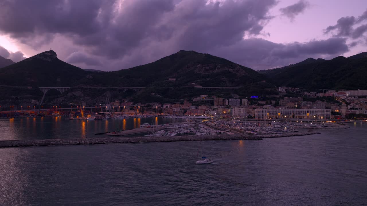 Drone che si allontana ruotando da una barca a vela di fronte al porto turistico di Salerno, crepuscolo in Italia