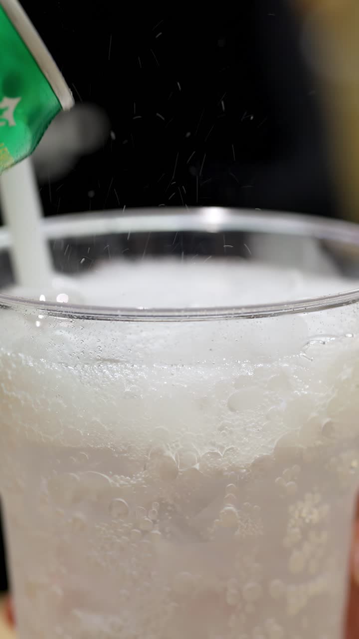 Bibita gassata versata in un bicchiere trasparente pieno di ghiaccio, primissimo piano con bollicine che salgono.