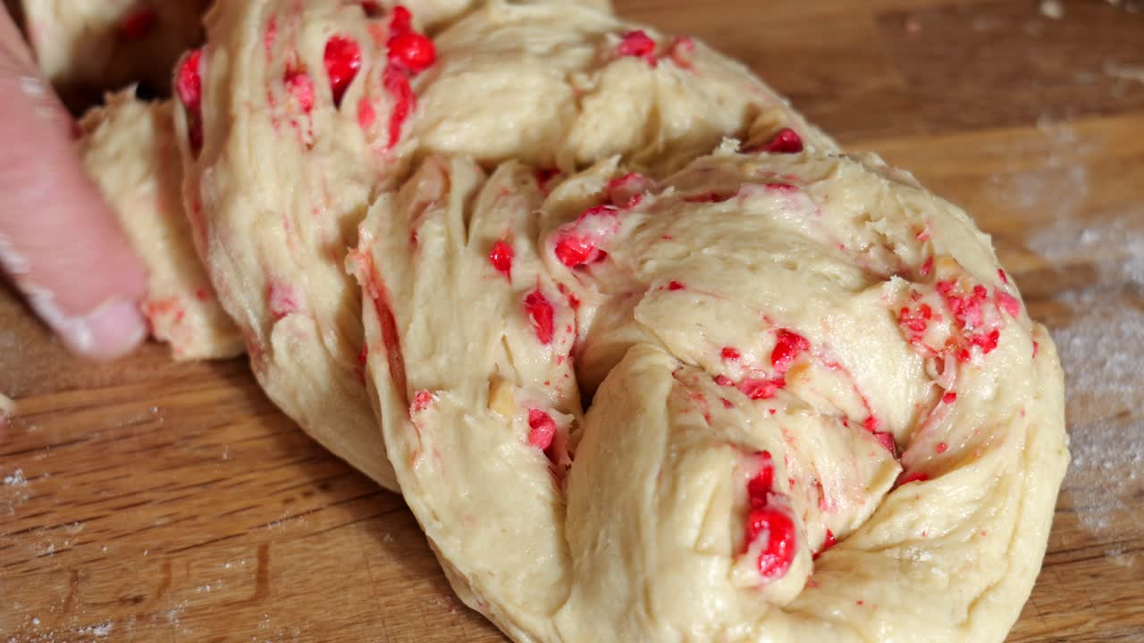 Primo piano di un fornaio che intreccia un impasto per dolci mescolato con praline rosse.
