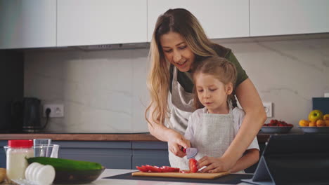madre enseña a la niña en delantal a cortar tomate en la mesa