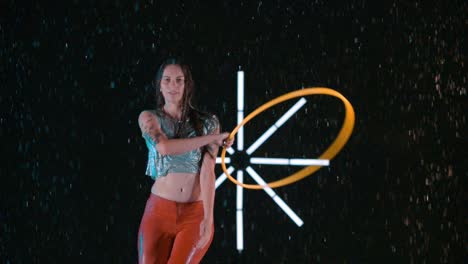 female hula hooping performing acrobatic skills in wet rain studio