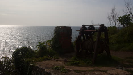 Mirando-El-Viejo-Equipo-De-Malacate-Oxidado-Del-Pescador-Con-La-Ciudad-Al-Fondo,-Cornwall