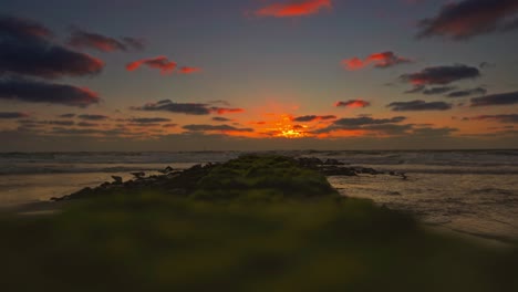 las olas vienen junto a un espigón en una playa al atardecer, crepúsculo rojo brillante en el horizonte