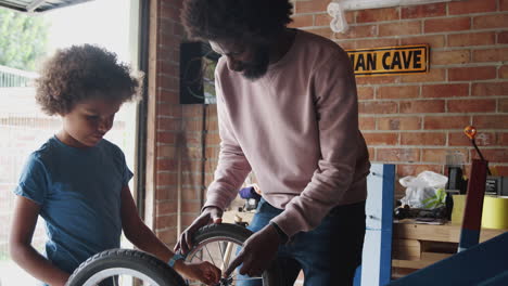 Middle-aged-father-and-pre-teen-son-standing-at-a-workbench-building-a-racing-kart-together-in-their-garage,-close-up,-waist-up