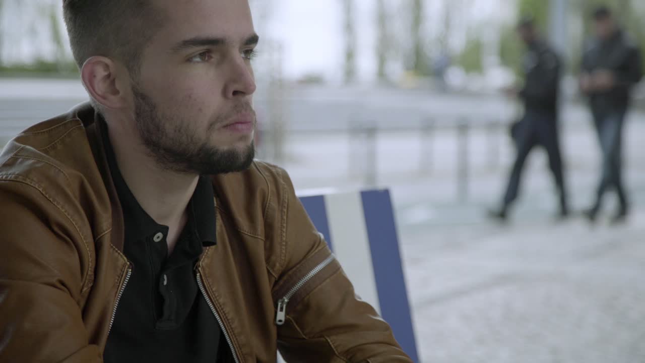 joven molesto sentado en un banco de madera y frotando la cabeza