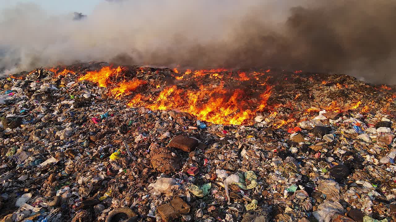 Closeup of burning landfill with fire spreading and smoke rising