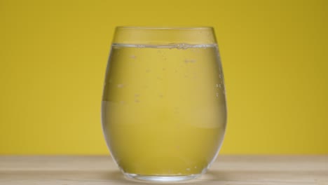 static shot of a clear drinking glass with sparkling water isolated on yellow