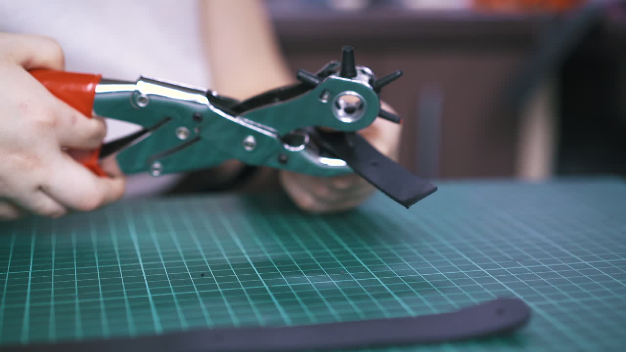 un sastre profesional hace agujeros en una tira de cuero negro.