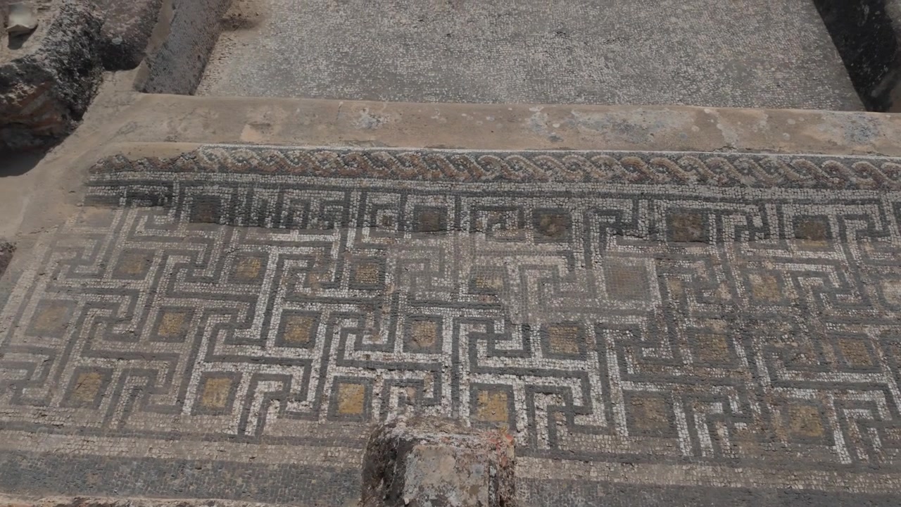 Vista cinematografica a livello del suolo di un mosaico geometrico romano conservato presso il sito archeologico di Volubilis, patrimonio UNESCO, che mostra intricate decorazioni del pavimento e artigianato classico in Marocco.