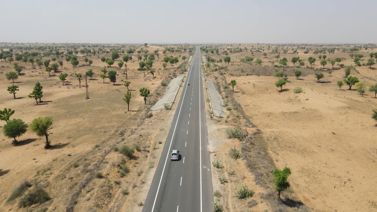 Aerial drone shot tracking a car as it drives between shifting sand dunes in Rajasthan’s desert.