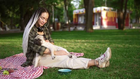 Chica-Con-Rastas-Sentada-En-Una-Manta-En-El-Césped-De-Un-Parque