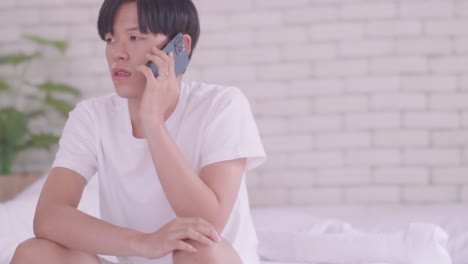 worried asian young man sitting in bed using cell phone.
