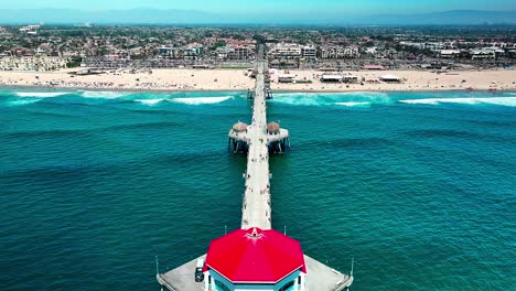 Vista-Aérea-Sobre-El-Muelle-En-Huntington-Beach,-California,-Con-Algunas-Personas-Caminando-Y-Una-Vista-Fresca-Del-Océano-Pacífico-Y-La-Playa-Y-El-Surf.