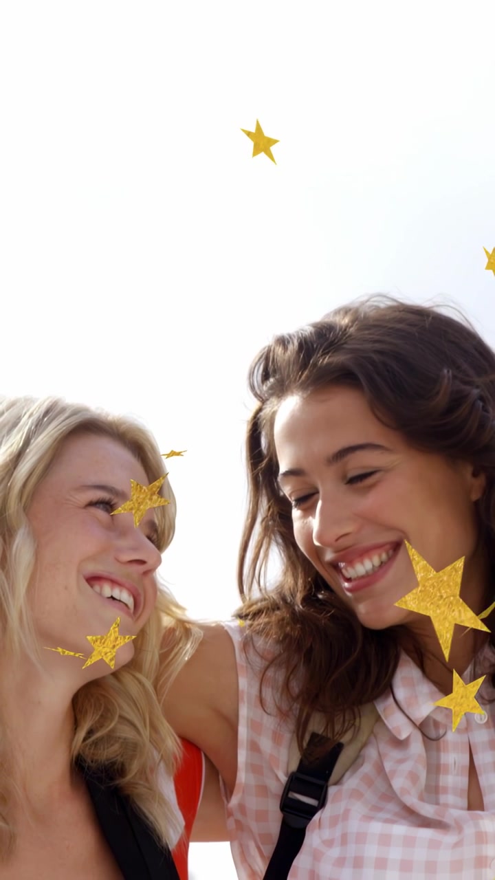 Vídeo vertical: Sorrisos com estrelas douradas cintilantes flutuando sobre duas mulheres inclinadas e rindo, para viagem.