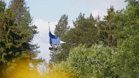 Flag-of-Finland-waving-among-tree-top-during-day-in-summer
