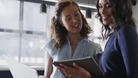 happy diverse female colleagues in discussion using tablet in casual office meeting, slow motion
