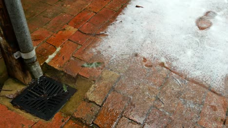 Wasser-Fließt-Aus-Einem-Fallrohr-In-Einen-Abfluss-Mit-Einem-Gemauerten-Weg-Und-Schnee