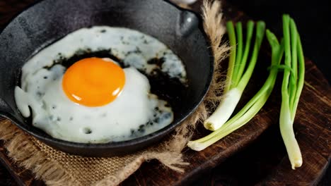 a frying pan with fried egg and green onions on the table.