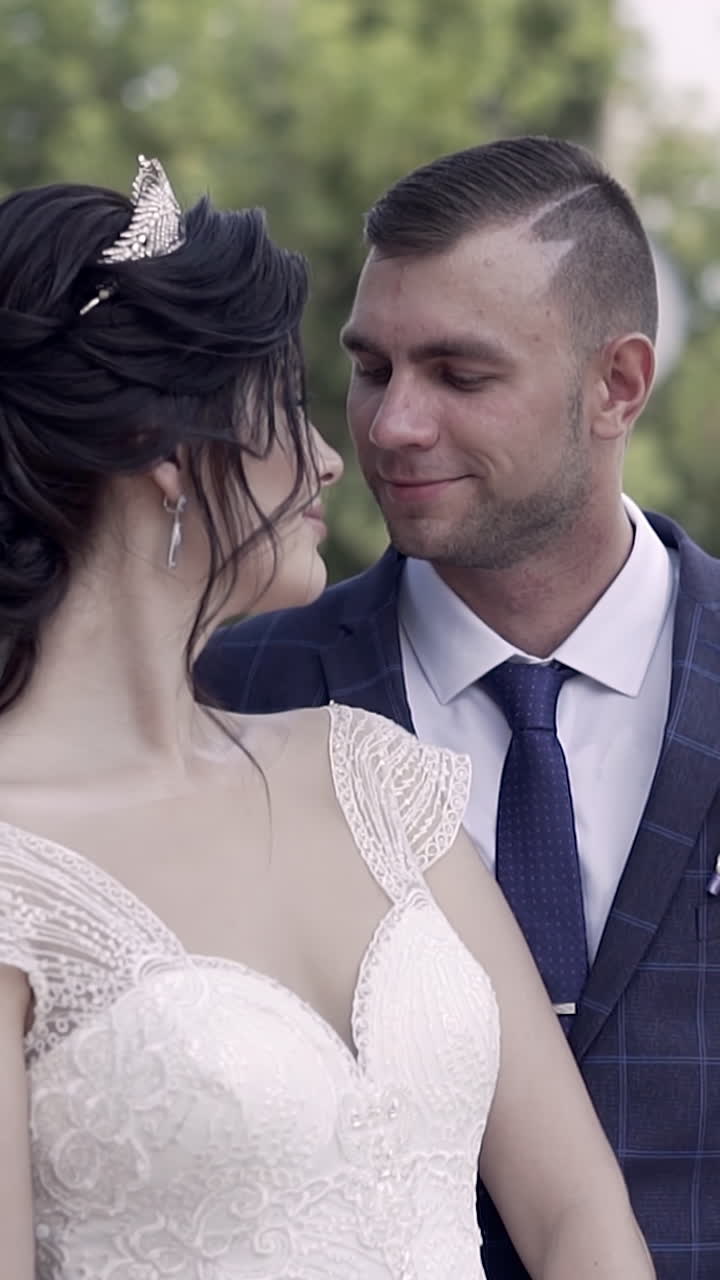 En cámara lenta, prometido sonriente abraza a maravillosa joven con vestido de novia y escote de encaje en un día soleado.