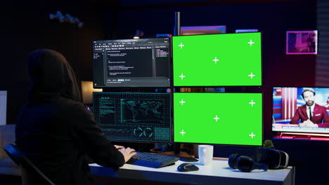 hooded man writing lines of code on green screen pc from apartment