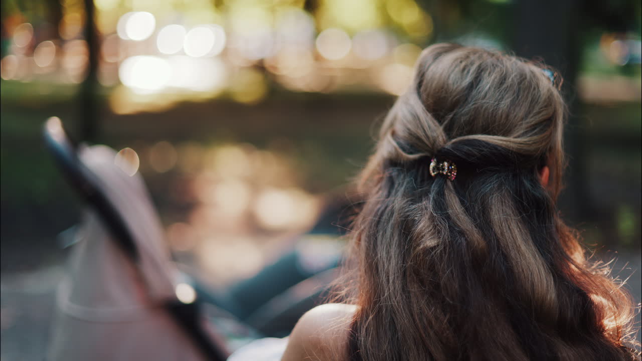 A mother with long wavy hair siting on a bench, breastfeeding her baby in a peaceful park, next to a modern baby stroller