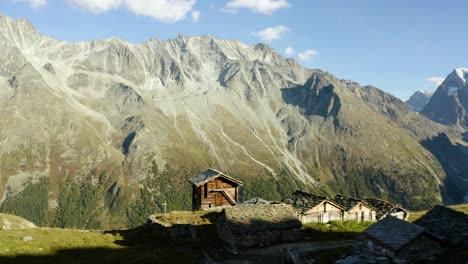 Flying-behind-small-"alpage"-chalets-with-high-mountain-peaks-in-the-background-Autumn-colors-in-Arolla,-Valais---Switzerland