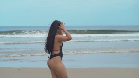 hispanic girl walks down the beach with waves crashing in the background and her hair flows in the wind