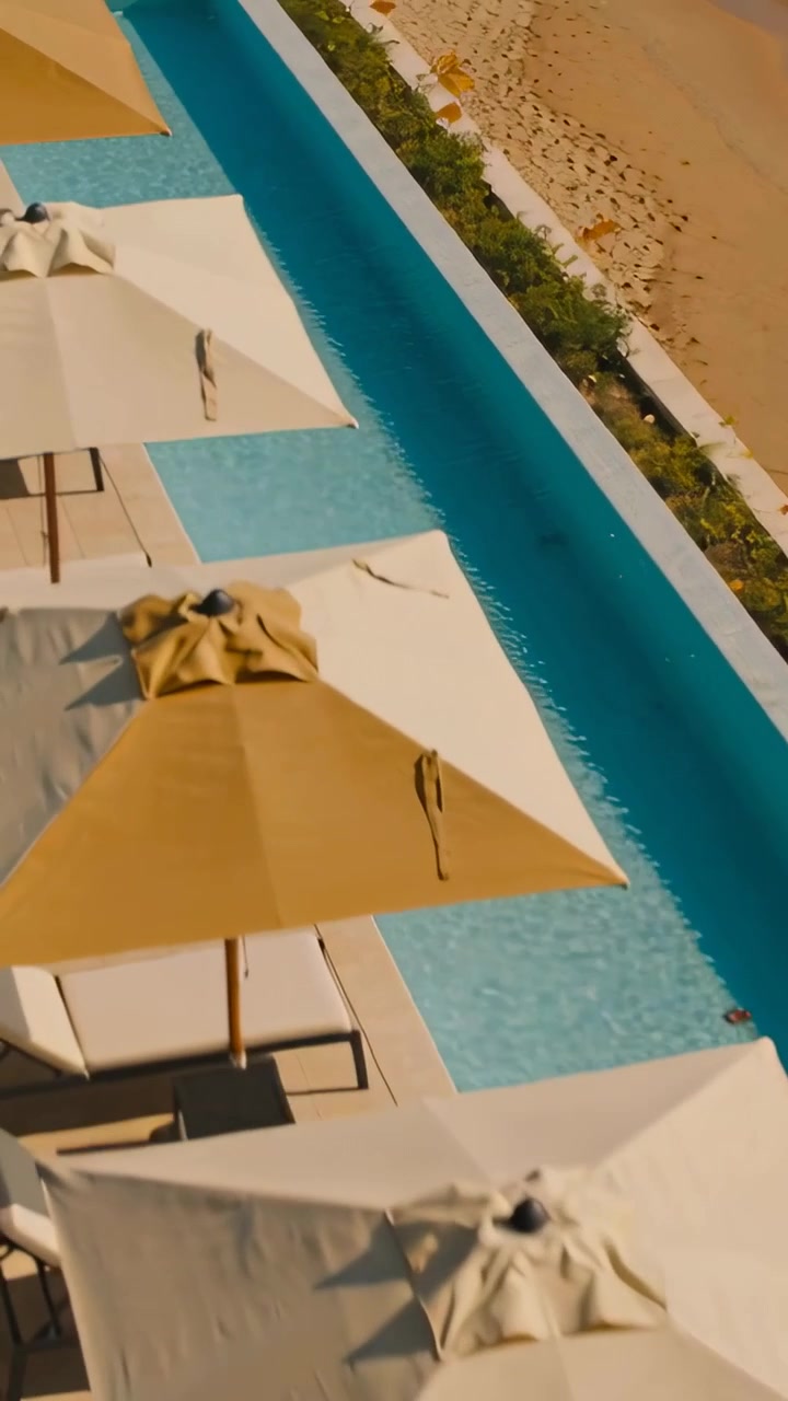 Vertical video: Panning camera revealing umbrella row and turquoise pool at beach, showing layout