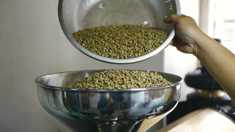 Freshly-dried-green-coffee-beans-being-poured-into-funnel-of-coffee-roasting-machine