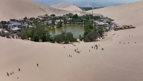 Desert-oasis-Huacachina,-Peru-with-lake-and-palms,-with-great-sand-dunes-in-the-background