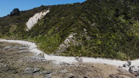 Mangawhai-Heads-aerial-shot-on-a-sunny-day,-flying-away-from-the-mountain-to-the-sea-showing-the-rocks-and-beach,-along-with-the-clear-view-of-the-mountain,-no-people