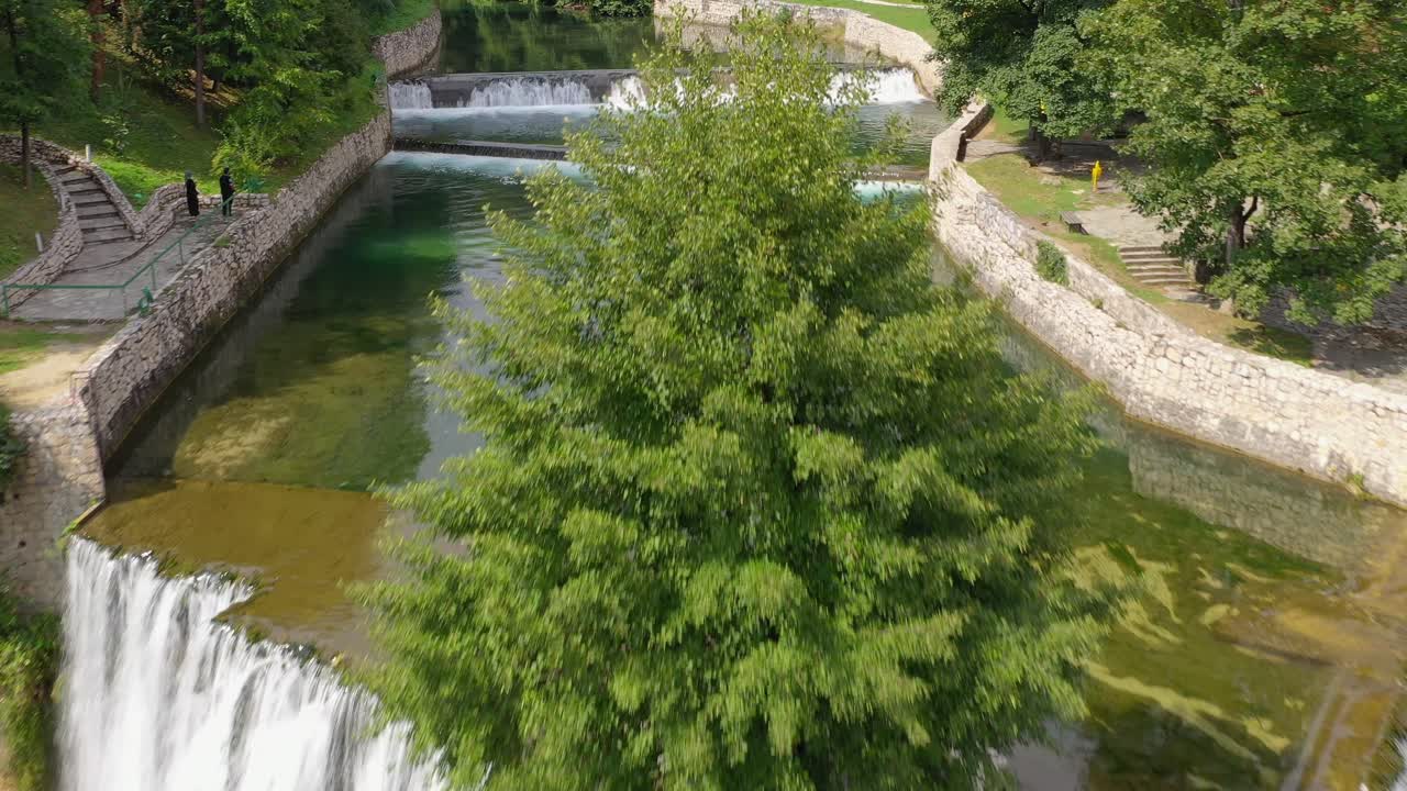 Jajce Waterfall in Bosnia and Herzegovina with tourists posing for pictures on the lookouts, Aerial flyover shot