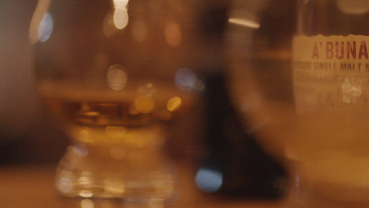 A slow, close-up camera pan reveals whiskey glasses on a wooden bar, with warm ambient lighting and a shallow depth of field