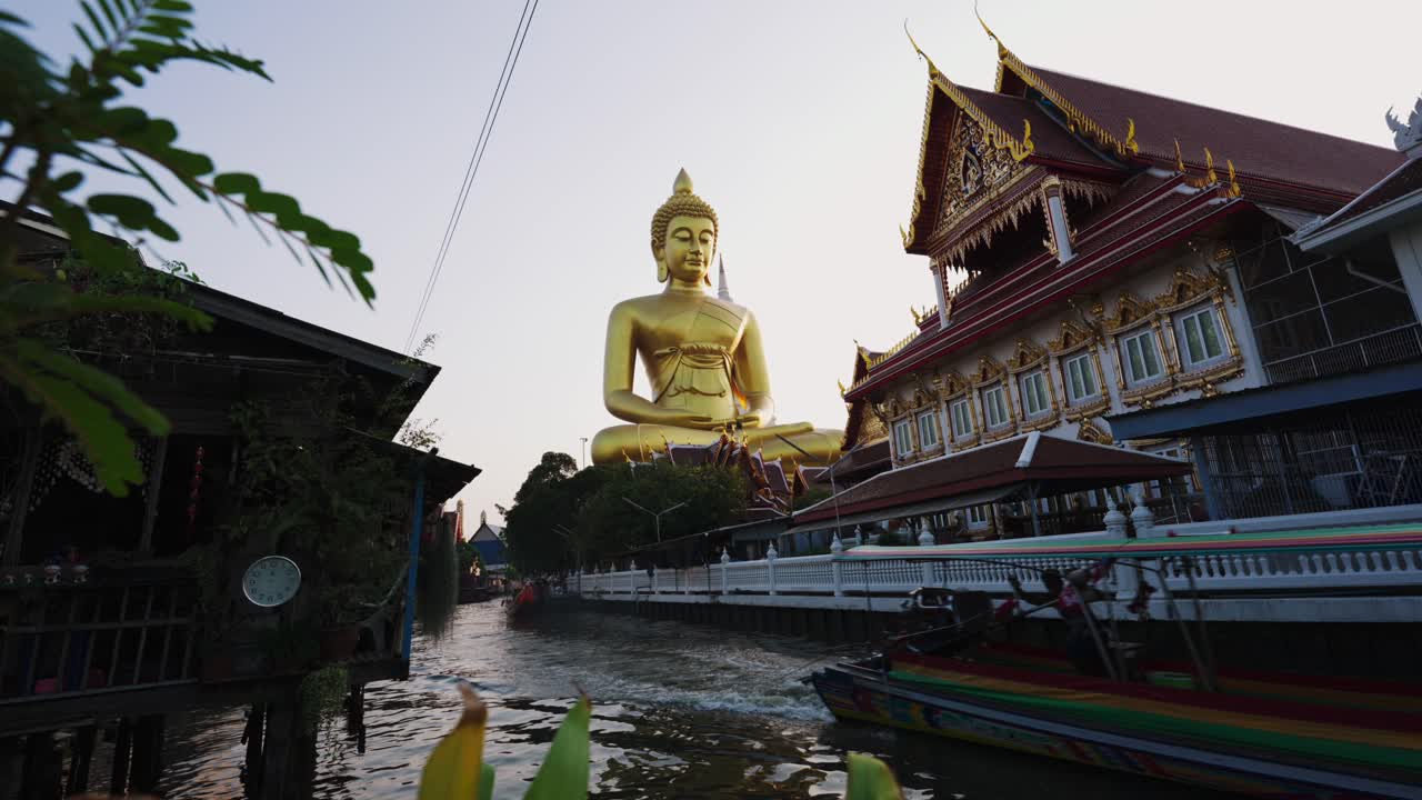 un impresionante primer plano de una magnífica estatua de buda de oro mientras un barco de cola larga pasa por el río tranquilo durante una fascinante puesta de sol