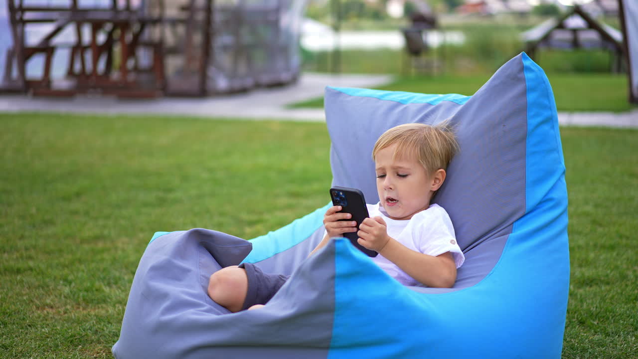 Bambino che usa uno smartphone su una poltrona a sacco all'aperto