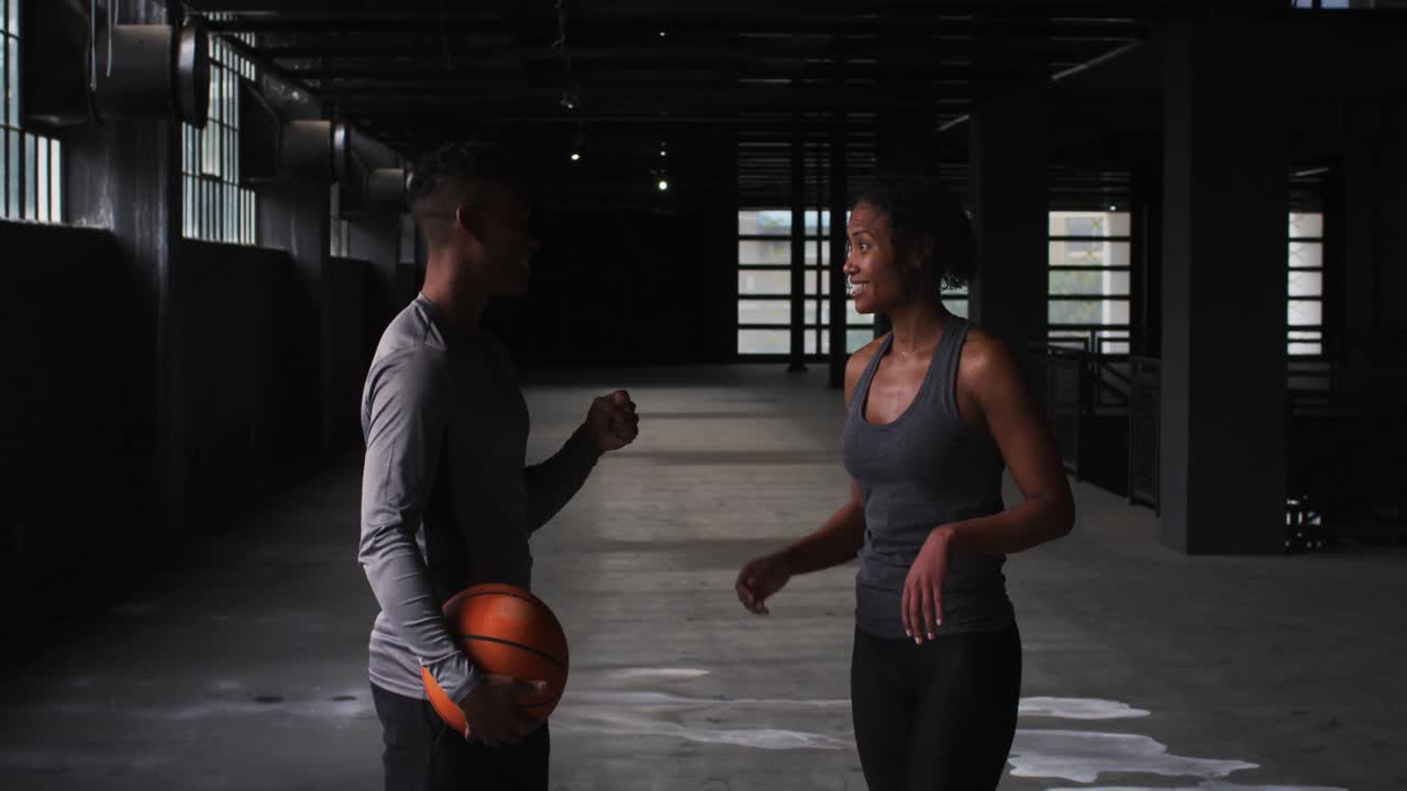 Uomo e donna afroamericani in piedi in un edificio vuoto che giocano con una palla da basket.