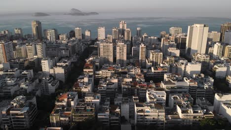 aerial upward movement showing ipanema neighbourhood in rio de janeiro with high rise and low rise buildings revealing islands just outside the coastline at sunrise