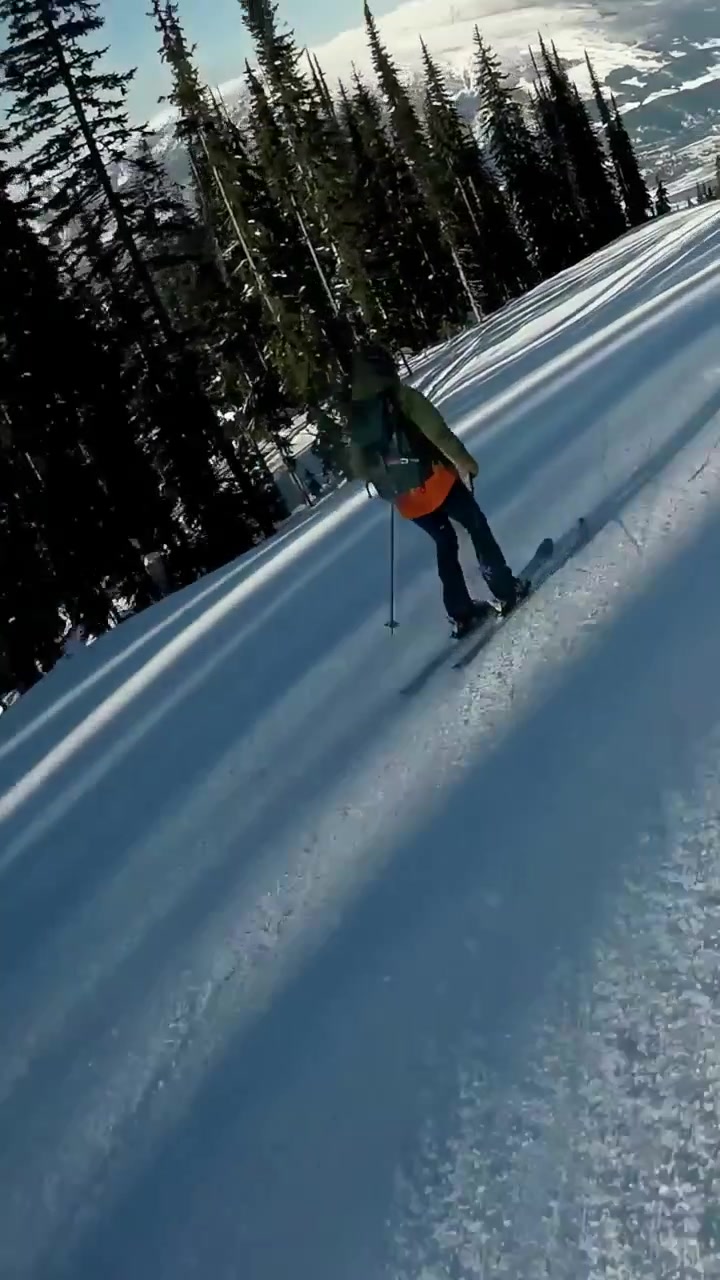 Video verticale: La telecamera segue uno snowboarder in giacca rossa che scende con curve ampie, uno sciatore in verde, con spazio per il testo.