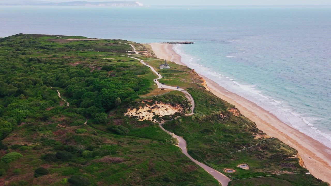 Drohnenaufnahme entlang Hengistbury Head mit Sandstrand, türkisfarbenem Meer, Küstenwanderwegen, Heidelandschaft, Wald, Dünen und Steinbuhne an der Küste von Dorset.
