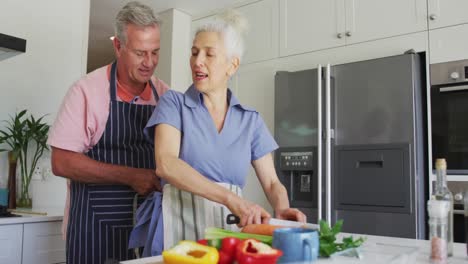pareja de alto nivel caucásica con delantales cocinando juntos en la cocina