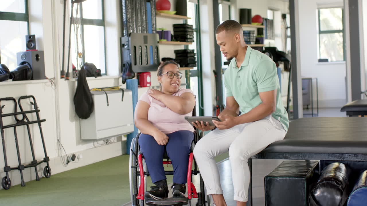 In rehabilitation center, showing tablet to woman with paraplegia in wheelchair, discussing therapy