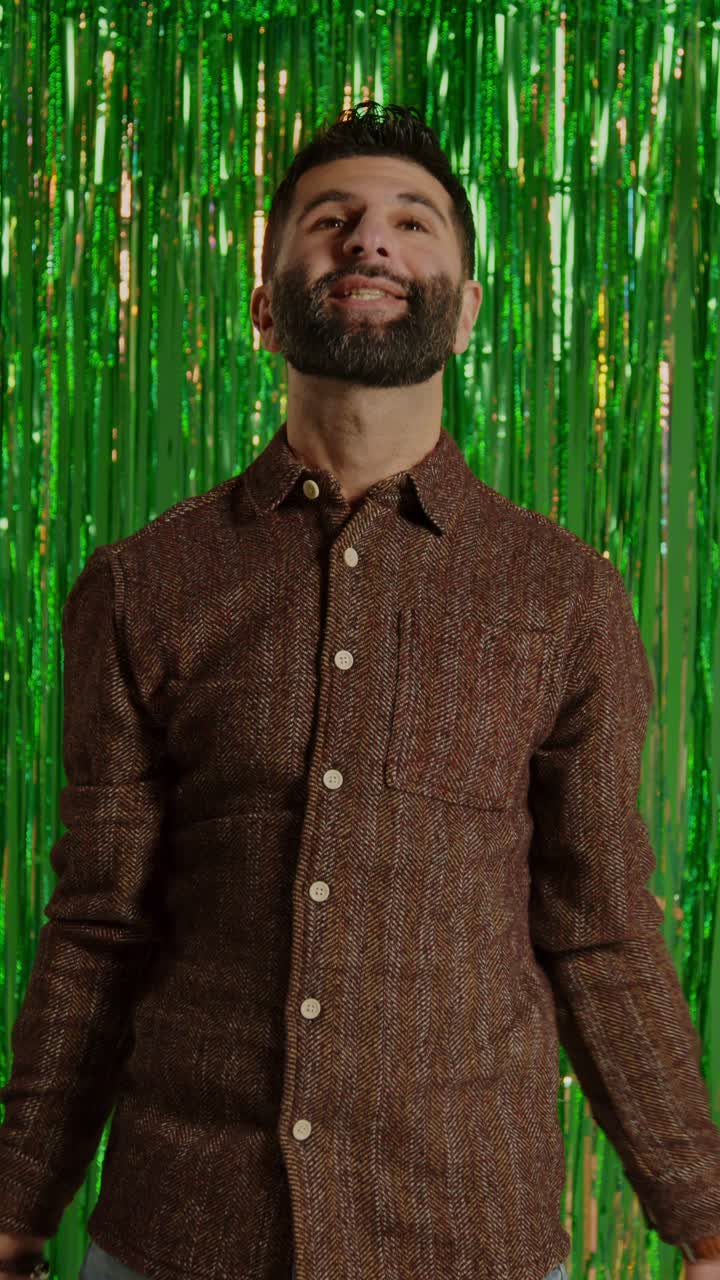 video vertical de un hombre celebrando el día de san patricio de pie frente a una cortina de oropel verde y arrojando monedas de oro novedosas en el aire