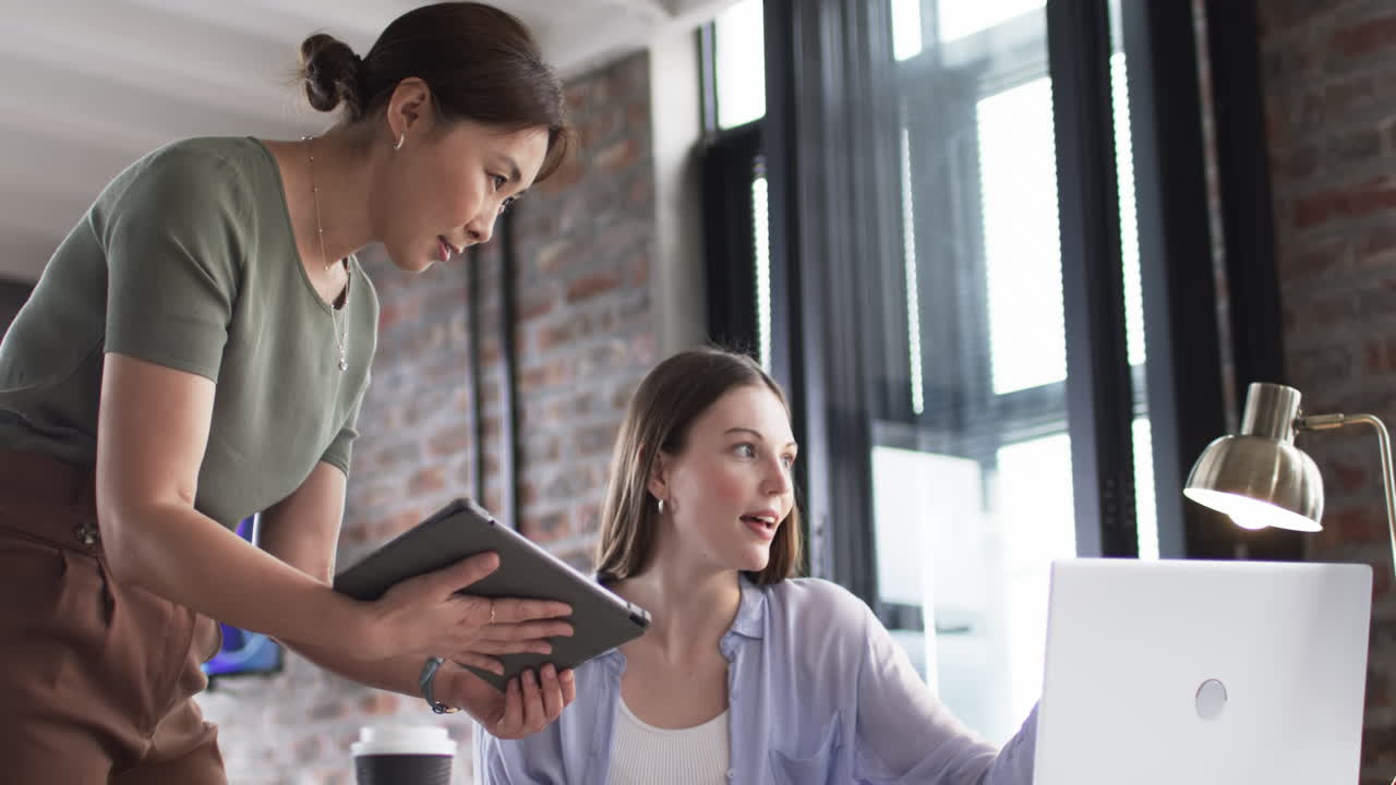 joven mujer caucásica y mujer asiática colaboran en una computadora portátil en una oficina de negocios