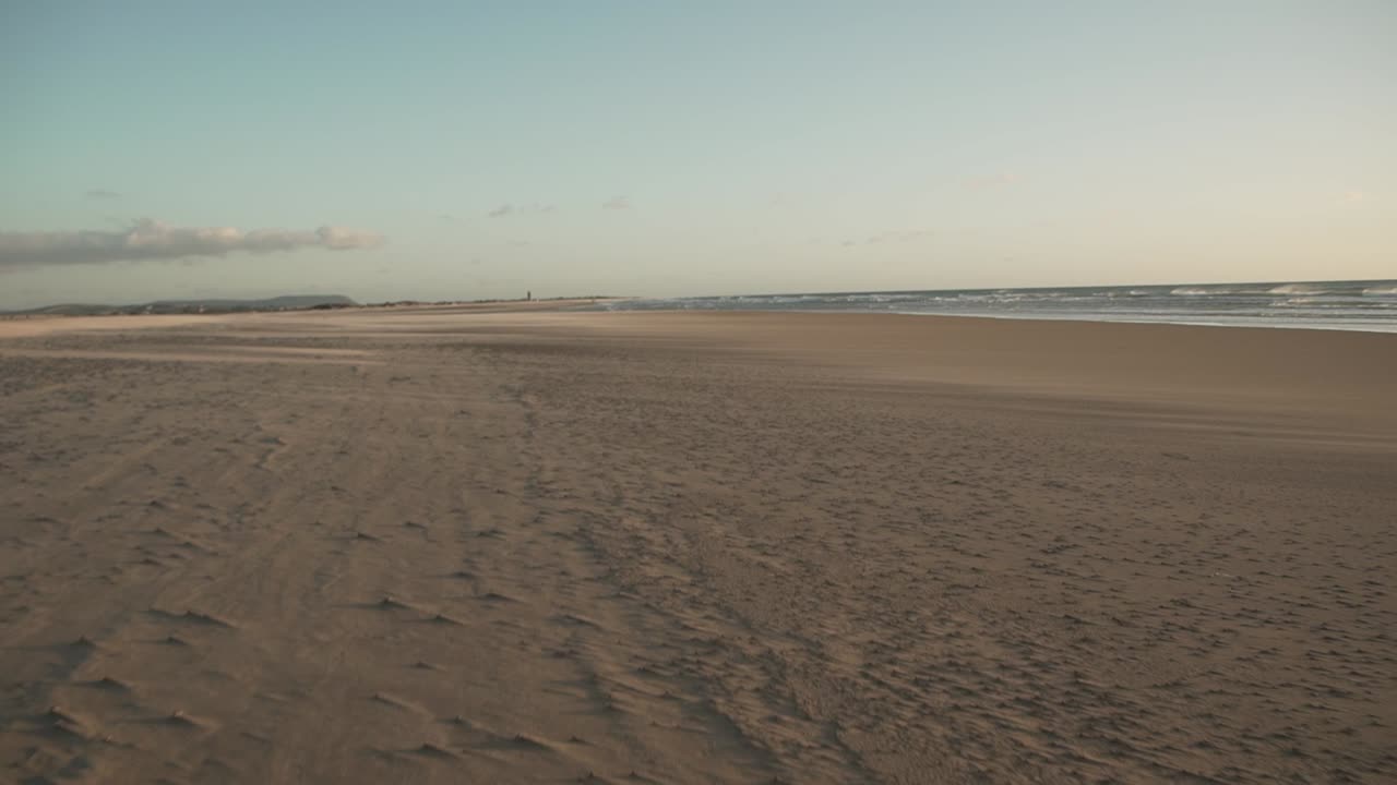 Kvinde løber på sandstrand på blæsende dag.