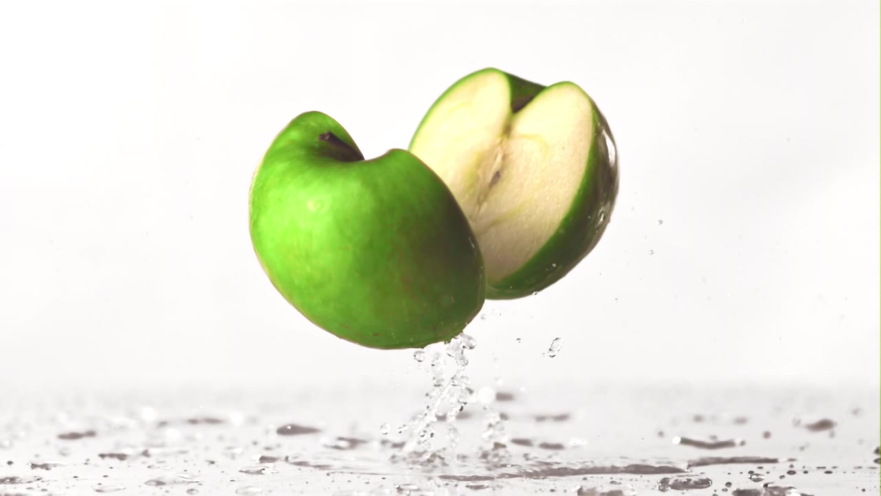 Mela verde fresca che si divide a metà con uno schizzo d'acqua.